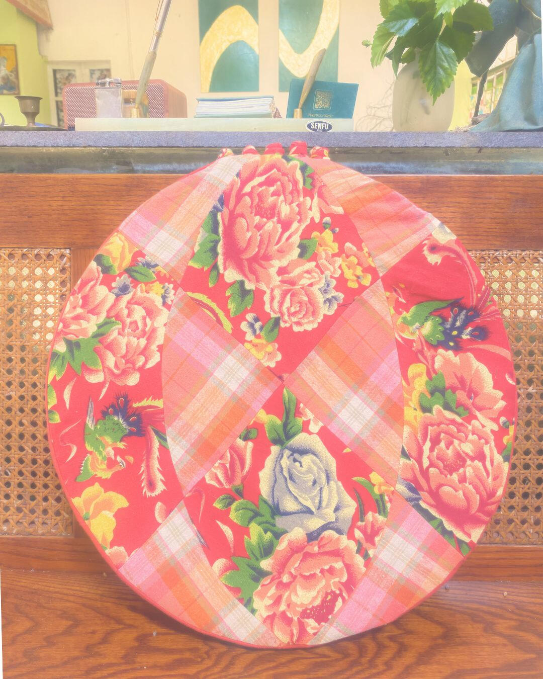 Circular textile cushion displayed upright against a wooden bench.