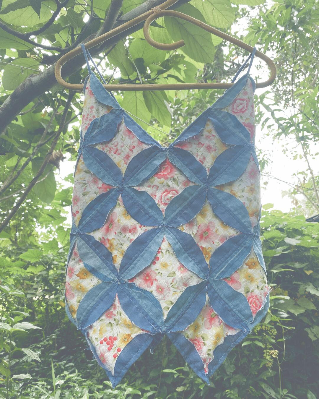 Patchwork vest displayed on a bamboo hanger outdoors.