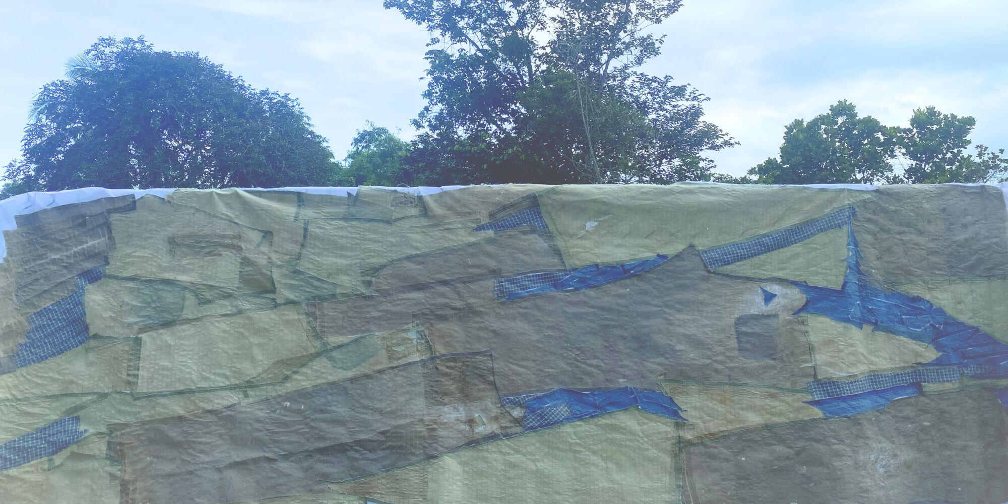 Suspended textile installation displayed against blue sky and trees.